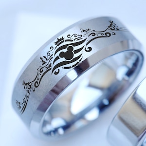 Puede incluir: Dos alianzas de plata con un dise&ntilde;o grabado en negro. Una alianza presenta una cabeza de Mickey Mouse y un dise&ntilde;o de ola estilizado.