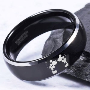 May include: Black tungsten carbide ring with a silver beveled edge and a laser engraved image of Mickey Mouse and Minnie Mouse holding hands. The ring is engraved with the words "Tungsten Carbide".
