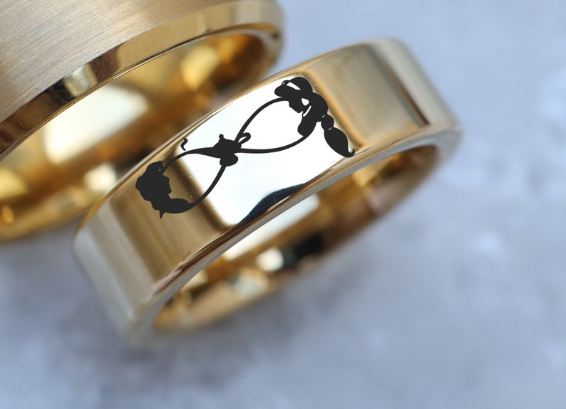 May include: Two gold wedding bands, one with a brushed finish and the other with a polished finish. The polished band has an infinity symbol engraved on it.