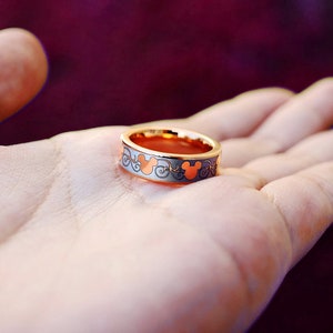 May include: A gold ring with a Mickey Mouse design. The ring is on a person's hand.