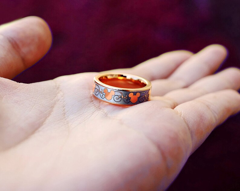 May include: A gold ring with a Mickey Mouse design. The ring is on a person's hand.