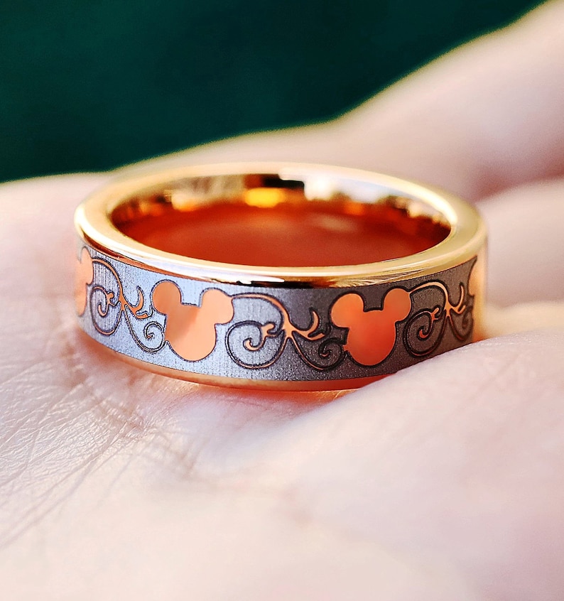 May include: A gold ring with a silver band and a pattern of Mickey Mouse heads and swirls.