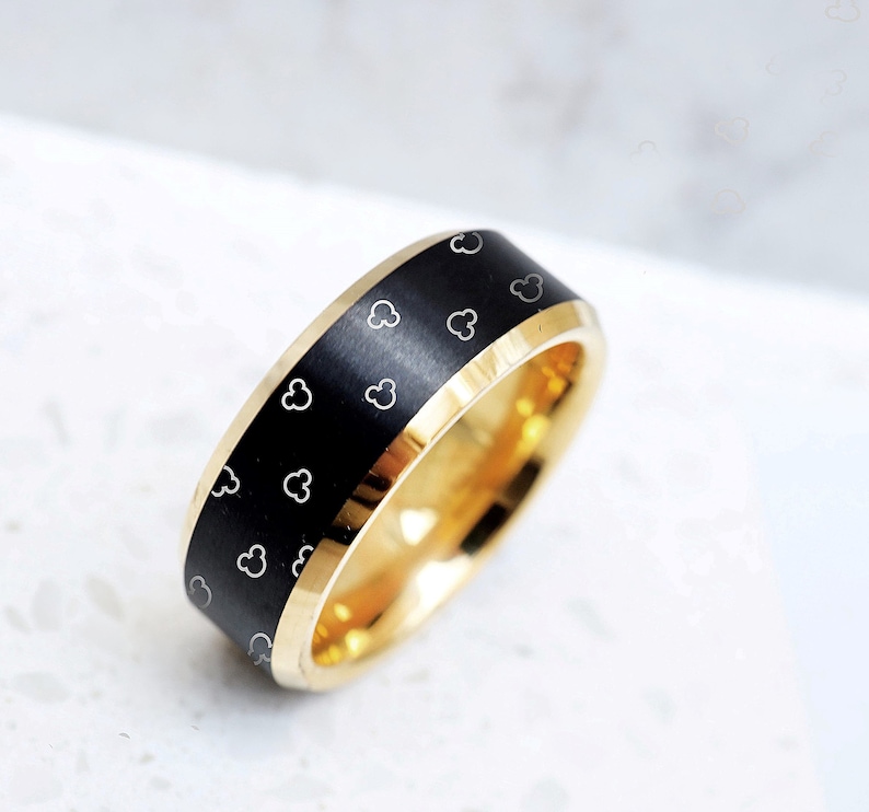 May include: A black and gold wedding band with a brushed finish and a pattern of small white Mickey Mouse heads.