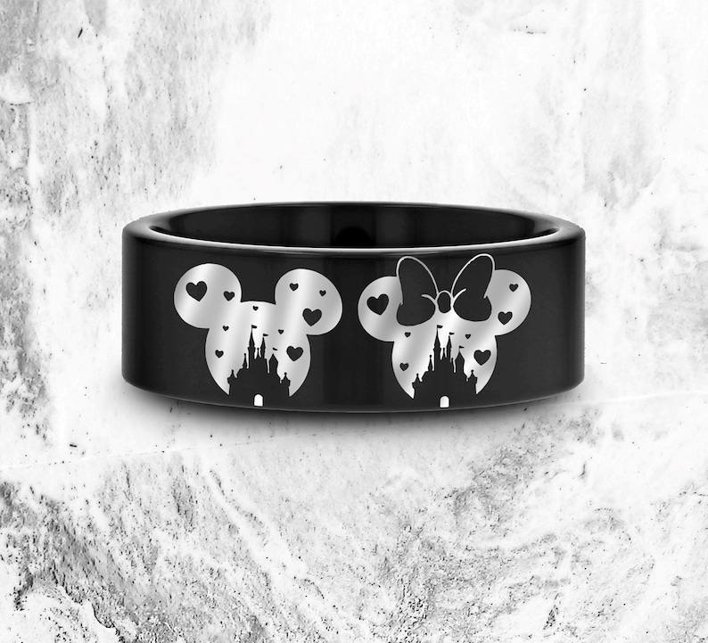 May include: A black ring with a silver Mickey Mouse and Minnie Mouse design. The design features the iconic Disney castle with hearts in the background.