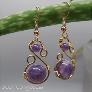 May include: A pair of gold wire earrings with amethyst gemstones. The earrings feature a swirling design with two amethyst beads on each earring.