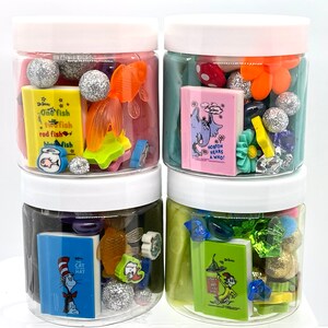 May include: Four clear plastic jars filled with colorful sensory play materials. Each jar contains glittery balls, small Dr. Seuss book replicas, and various themed embellishments. The jars have white lids and are arranged in a stack.