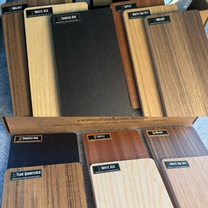May include: A close-up of wood samples in various colors and grains, including walnut, white ash, smoked oak, sapele, and teak. The samples are arranged in two rows, with the top row showing the wood in its natural state and the bottom row showing the wood after it has been finished. The text "ewwoodcraft.com/design" is printed on the box.