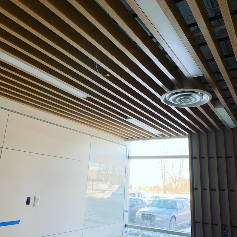 May include: A modern office space with a wood slat ceiling and a large window. The ceiling has a circular air vent and a white wall with a light switch.