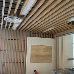 May include: A room with a wooden slat ceiling and a white wall with a rectangular opening. The opening is covered with a piece of plywood.