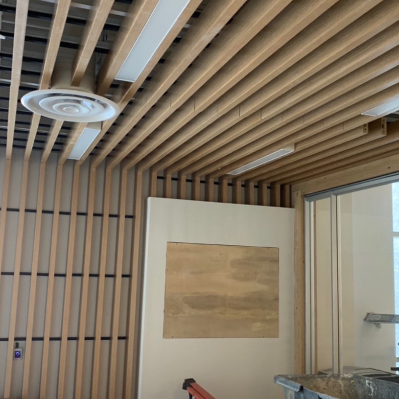 May include: A room with a wooden slat ceiling and a white wall with a rectangular opening. The opening is covered with a piece of plywood.