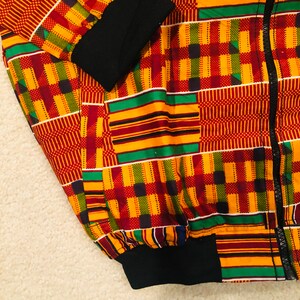 Puede incluir: Una chaqueta bomber de color rojo, amarillo, verde y negro con cierre de cremallera. La chaqueta tiene un cuello, pu&ntilde;os y cintura de canal&eacute; negros.