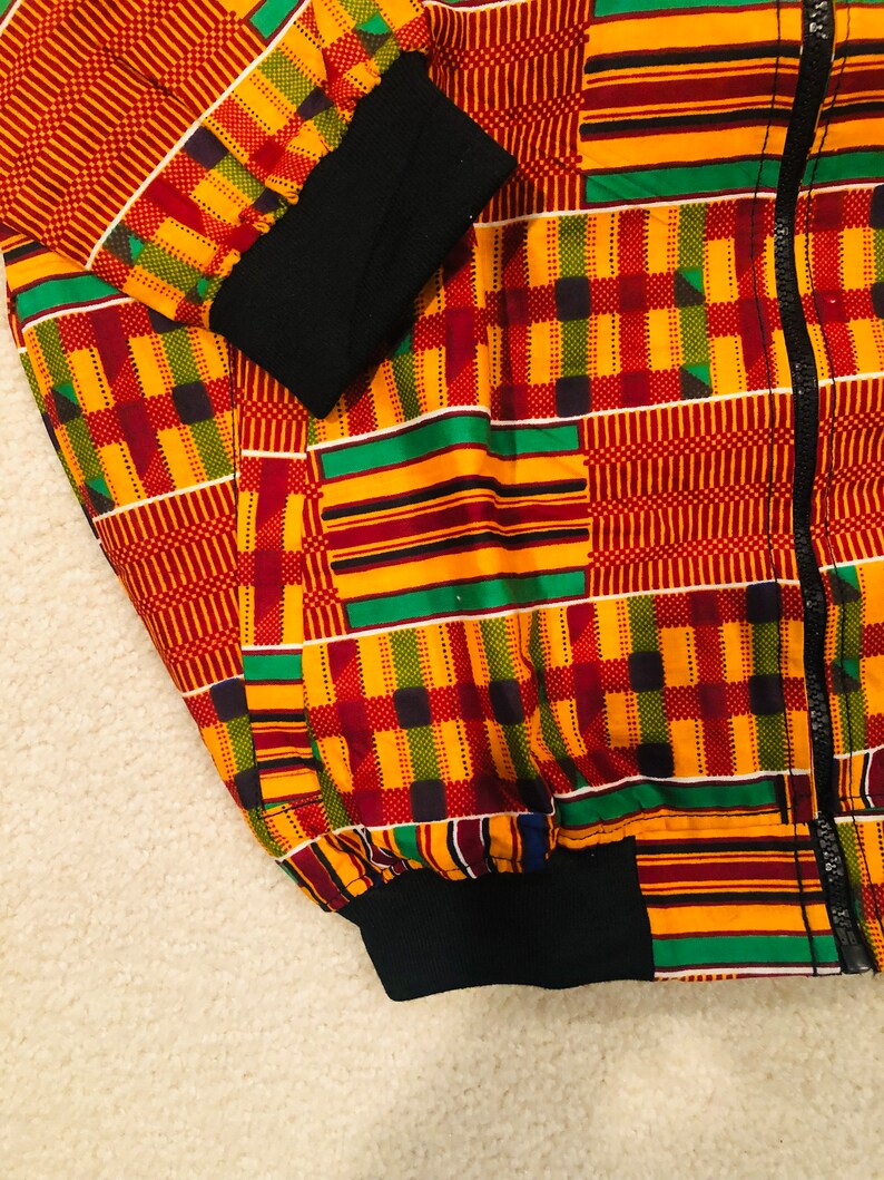 Puede incluir: Una chaqueta bomber de color rojo, amarillo, verde y negro con cierre de cremallera. La chaqueta tiene un cuello, pu&ntilde;os y cintura de canal&eacute; negros.