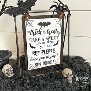 May include: Black and white printable sign with the text "trick or treat take a sweet two or three if you dare but please leave some to spare! happy halloween!"  The sign is on a black metal easel with a spider and bat decoration.