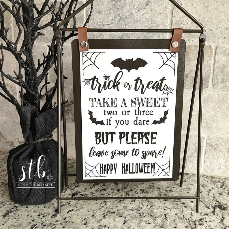 May include: Black and white sign with the text "trick or treat take a sweet two or three if you dare but please leave some to spare! happy halloween!" on a black background with a bat and spiderwebs.