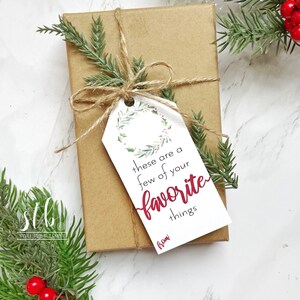 May include: A white gift tag with a green wreath and red berries. The tag says "these are a few of your favorite things" in black text and "from" in red text. The tag is tied to a brown gift box with twine.