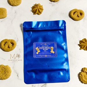 May include: A blue resealable pouch with a label that reads "Cinnamon Spice Wax Melts". The pouch is on a white surface with several small cookies.