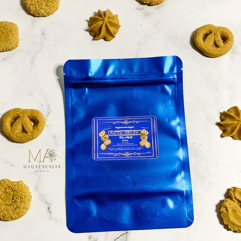 May include: A blue resealable pouch with a label that reads "Cinnamon Spice Wax Melts". The pouch is on a white surface with several small cookies.
