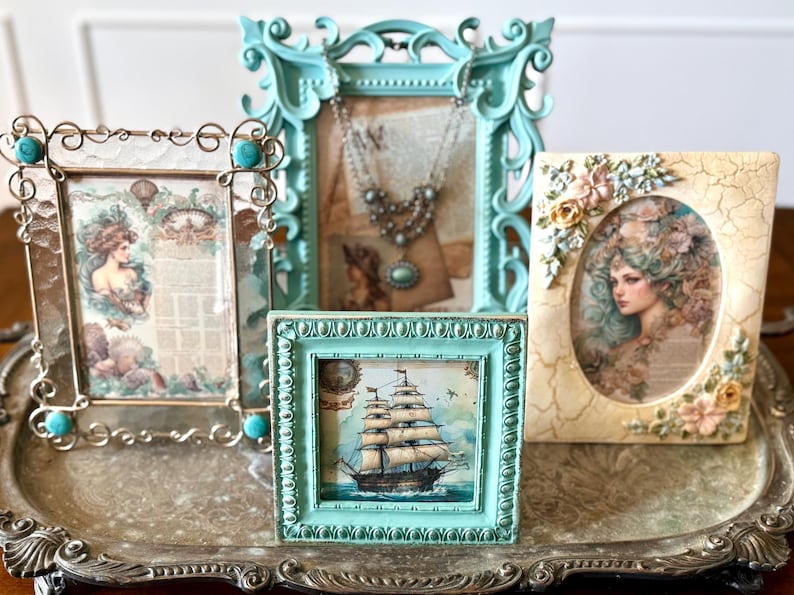 May include: An assortment of decorative picture frames in various sizes and styles. The frames are in shades of teal, silver, and cream, with ornate details and vintage-style artwork. The frames are arranged on a decorative silver tray.
