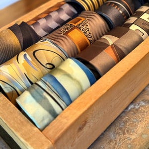 Puede incluir: Un juego de tres tazas de cerámica con un esmalte moteado de color crema. Cada taza presenta un diseño pintado a mano diferente: una hoja azul y verde, una flor amarilla y naranja y una ramita de bayas rojas. Las tazas tienen una forma simple y redondeada.