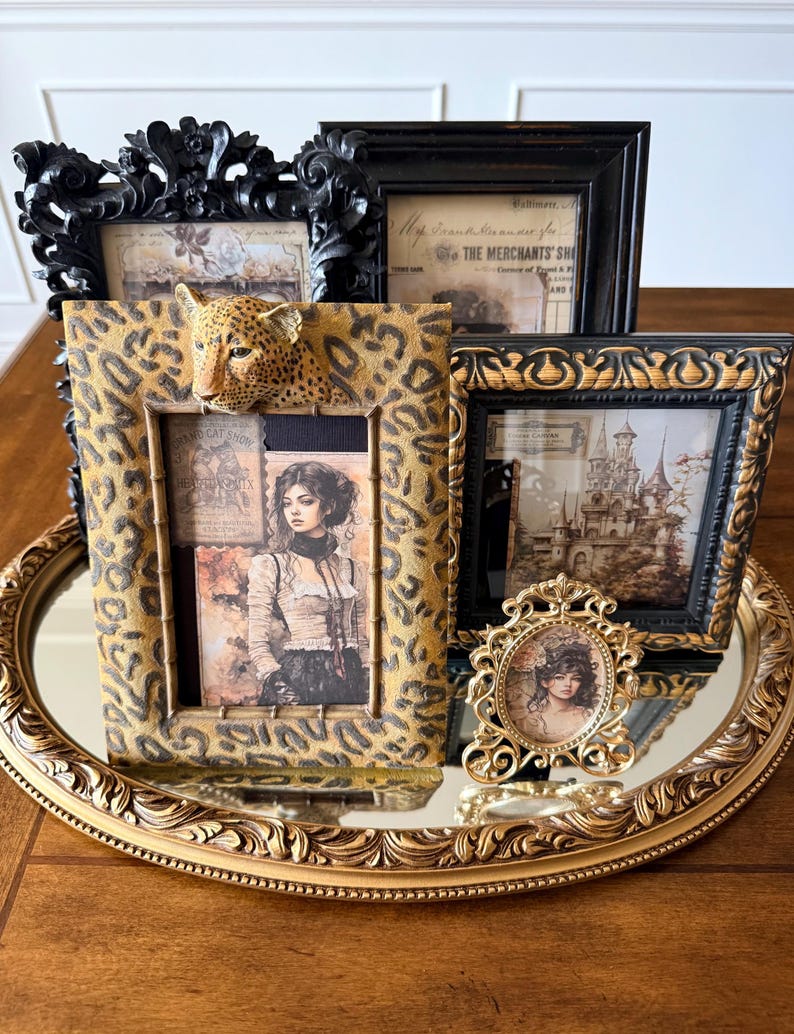 May include: An assortment of decorative picture frames in various styles. Includes a leopard print frame with a 3D leopard head, ornate black frames, and a small gold oval frame. The frames are displayed on a gold-toned, oval tray.
