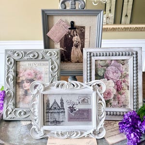 May include: A collection of ornate picture frames in various sizes and styles. The frames are in shades of gray and white, with decorative details. The framed images include vintage photographs and floral prints, creating a romantic and antique aesthetic.