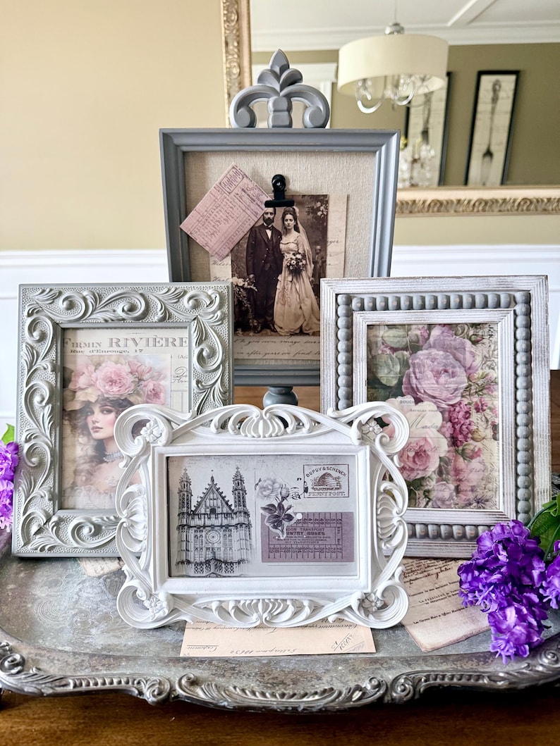 May include: A collection of ornate picture frames in various sizes and styles. The frames are in shades of gray and white, with decorative details. The framed images include vintage photographs and floral prints, creating a romantic and antique aesthetic.