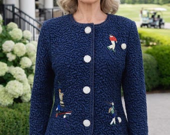 May include: A woman wearing a navy blue textured jacket with white buttons and embroidered golf-themed designs. The jacket is paired with white pants. A golf course and cart are visible in the background.
