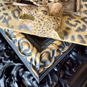 May include: Close-up of decorative picture frames. One frame has a leopard print design with a sculpted leopard head. Another frame is black with gold accents and ornate carvings. A third frame is gold with an oval shape.