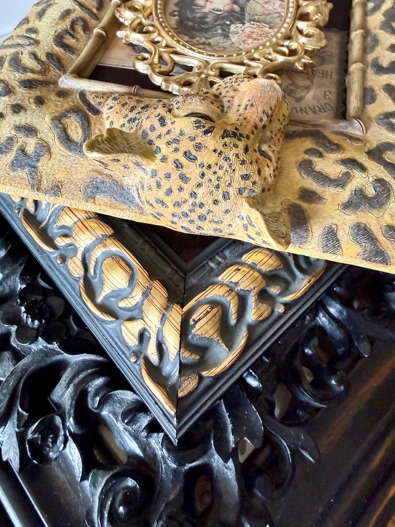 May include: Close-up of decorative picture frames. One frame has a leopard print design with a sculpted leopard head. Another frame is black with gold accents and ornate carvings. A third frame is gold with an oval shape.