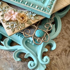 May include: An assortment of decorative frames and a silver pendant with a turquoise stone. The frames are in various styles, including a light blue ornate frame and a cream-colored frame with floral embellishments. The image features a nautical theme.