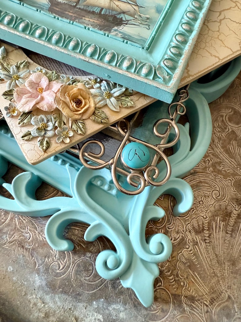 May include: An assortment of decorative frames and a silver pendant with a turquoise stone. The frames are in various styles, including a light blue ornate frame and a cream-colored frame with floral embellishments. The image features a nautical theme.