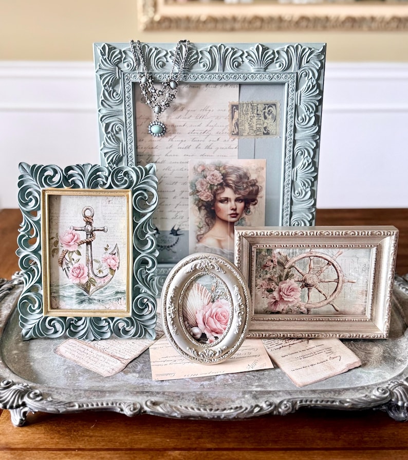 May include: A collection of ornate picture frames in various shapes and sizes, arranged on a decorative silver tray. The frames are in shades of blue and cream, with vintage-style artwork featuring roses, anchors, and a portrait. A silver necklace is draped over one frame.