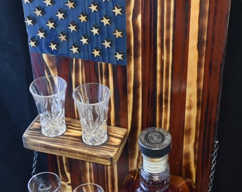 May include: A wooden wall-mounted bar with an American flag design. It features two shelves, one for shot glasses and one for a bottle of Jack Daniel's Single Barrel Select Tennessee Whiskey.