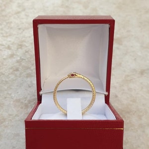 Op de afbeelding: Een gouden slangenring met een rode robijn oog, gepresenteerd in een rode fluwelen ringdoos.