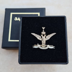 Puede incluir: Un pin de águila dorado con una corona y una pancarta que dice "Deus Meumque Jus". El pin está en una caja de terciopelo negro.
