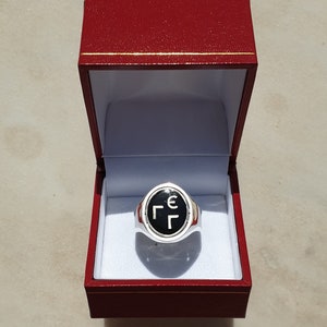 Puede incluir: Un anillo de plata con una piedra ovalada negra que presenta las letras griegas 'ΓΓΕ' en blanco.