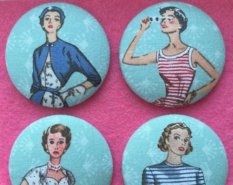 May include: Set of four round fabric pinback buttons featuring vintage illustrations of women in various outfits. Each button has a light blue background with a white border.
