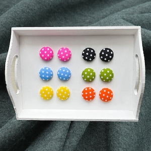 Op de afbeelding: Een set van 10 kleurrijke stippenstofknoppen in een witte lade. De knoppen zijn in verschillende kleuren, waaronder roze, blauw, groen, geel, zwart en oranje.