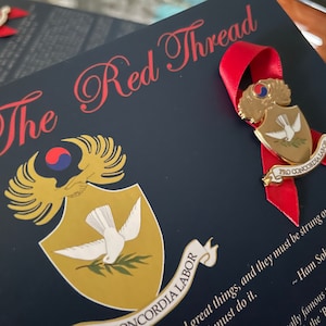 May include: A gold pin with a dove and olive branch, surrounded by a red ribbon with the text "Pro Concordia Labor" on a dark blue background with the text "The Red Thread".