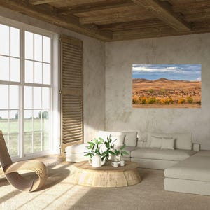 May include: A living room interior with a large window, a white sectional sofa, a wooden coffee table, and a framed landscape photograph of a field with trees and a cloudy sky.