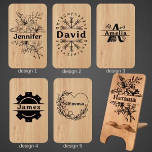Puede incluir: Soportes de teléfono de madera con diseños personalizados. Los diseños incluyen arreglos florales, nombres como "Jennifer", "David", "Amelia", "James", "Emma" y "Наташа", y otros elementos decorativos. Los soportes son de madera clara.
