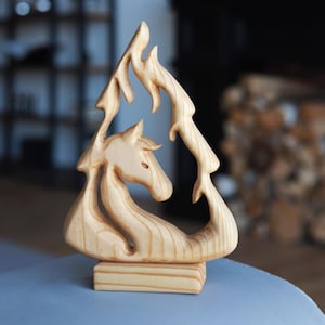 Peut inclure: Sculpture en bois clair représentant un cheval dans une forme de flamme stylisée. La sculpture est posée sur un socle rectangulaire. La tête du cheval est visible, et le motif de la flamme l'entoure.