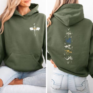 May include: An olive green hoodie with a front pocket and hood. The front features a white dragon design with a crescent moon. The back displays a vertical arrangement of dragon illustrations in white, blue, and gold.