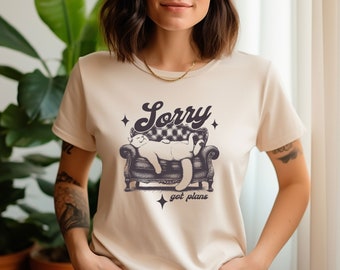 Könnte beinhalten: Ein beiges T-Shirt mit einem Aufdruck eines auf einem Sofa liegenden Katers. Der Text "Sorry got plans" ist unter dem Kater aufgedruckt.