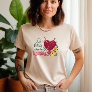 May include: A cream-colored t-shirt with a graphic of a red heart with knitting needles and yarn. The text "Life is better when I'm knitting" is printed below the heart.