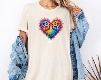May include: A cream-coloured t-shirt with a watercolour heart design featuring two paw prints. The heart is filled with vibrant colours, including blue, yellow, orange, and purple, with paint splatter effects. The shirt is a casual style.