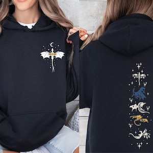 May include: Black hooded sweatshirt with a dragon design. The front features a white and gold dragon with a crescent moon and stars. The back displays a vertical arrangement of various dragon illustrations in white, blue, gold, and white.