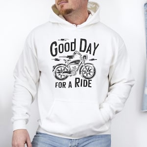 Może przedstawiać: Kremowa bluza z kapturem z czarnym nadrukiem graficznym przedstawiającym rower w stylu vintage na środku klatki piersiowej. Napis "GOOD DAY FOR A RIDE" jest wydrukowany pogrubioną, ciemną czcionką nad i pod ilustracją roweru z przodu.