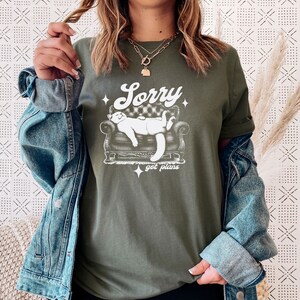 May include: A green t-shirt with a white graphic of a cat lounging on a couch. The text "Sorry got plans" is printed below the cat.