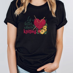 May include: Black t-shirt with the text "Life is better when I'm knitting" and a red yarn ball with knitting needles and flowers.